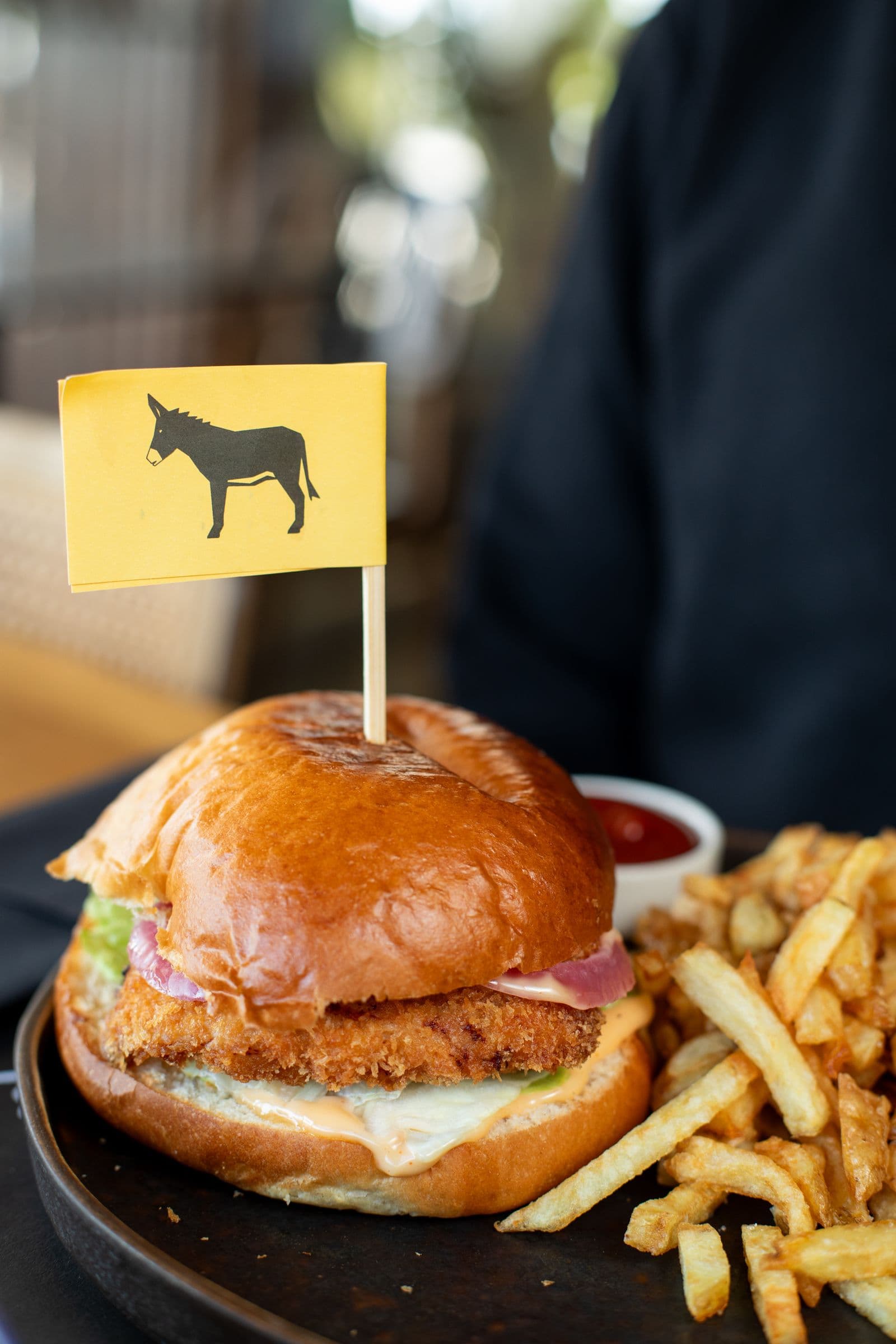 Burger Fried Chicken σε ψωμάκι brioche με κίτρινο σημαιάκι γαϊδουράκι και τηγανητές πατάτες