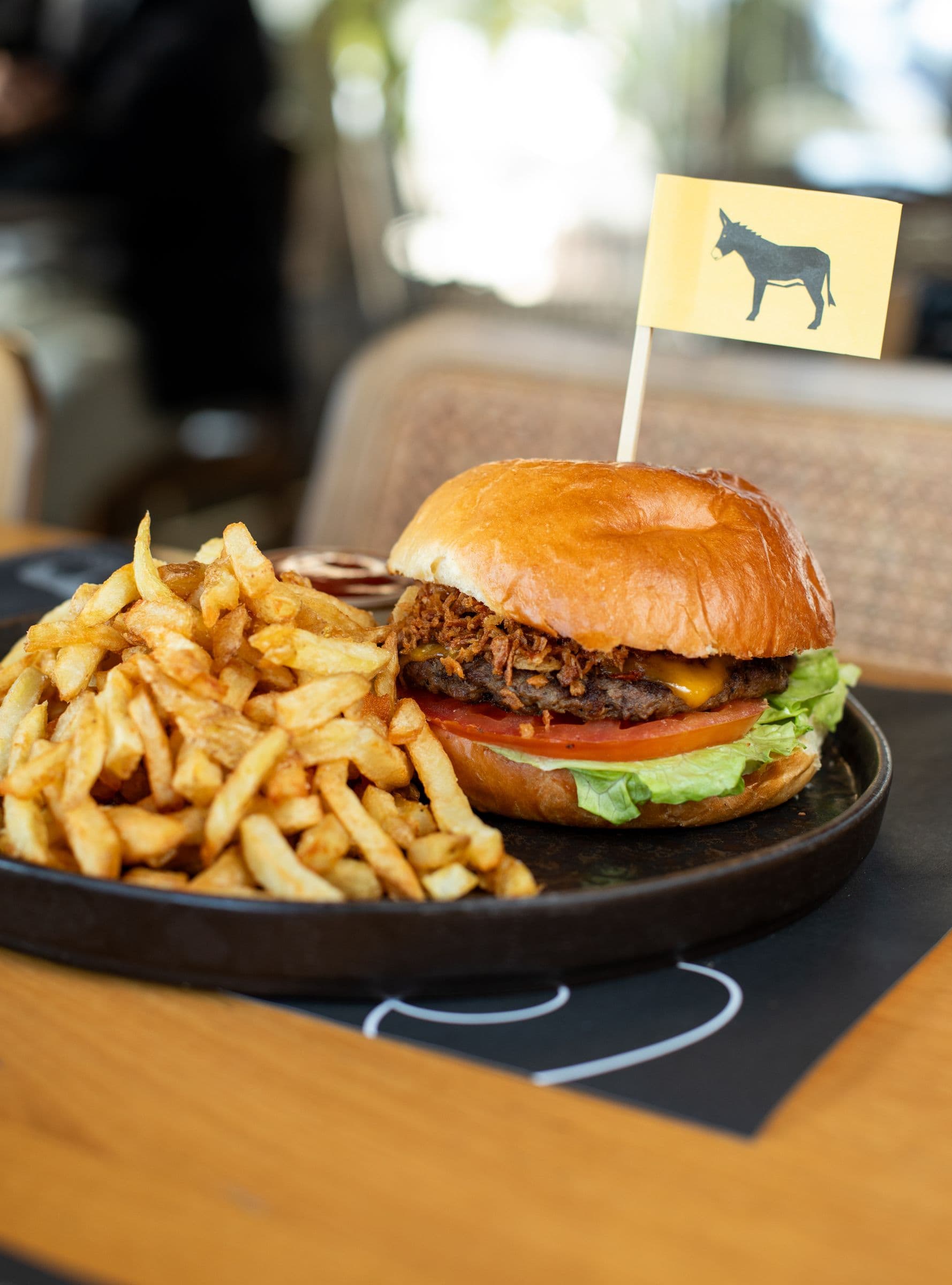 Burger από Black Angus με κίτρινο σημαιάκι γαϊδουράκι και τηγανητές πατάτες